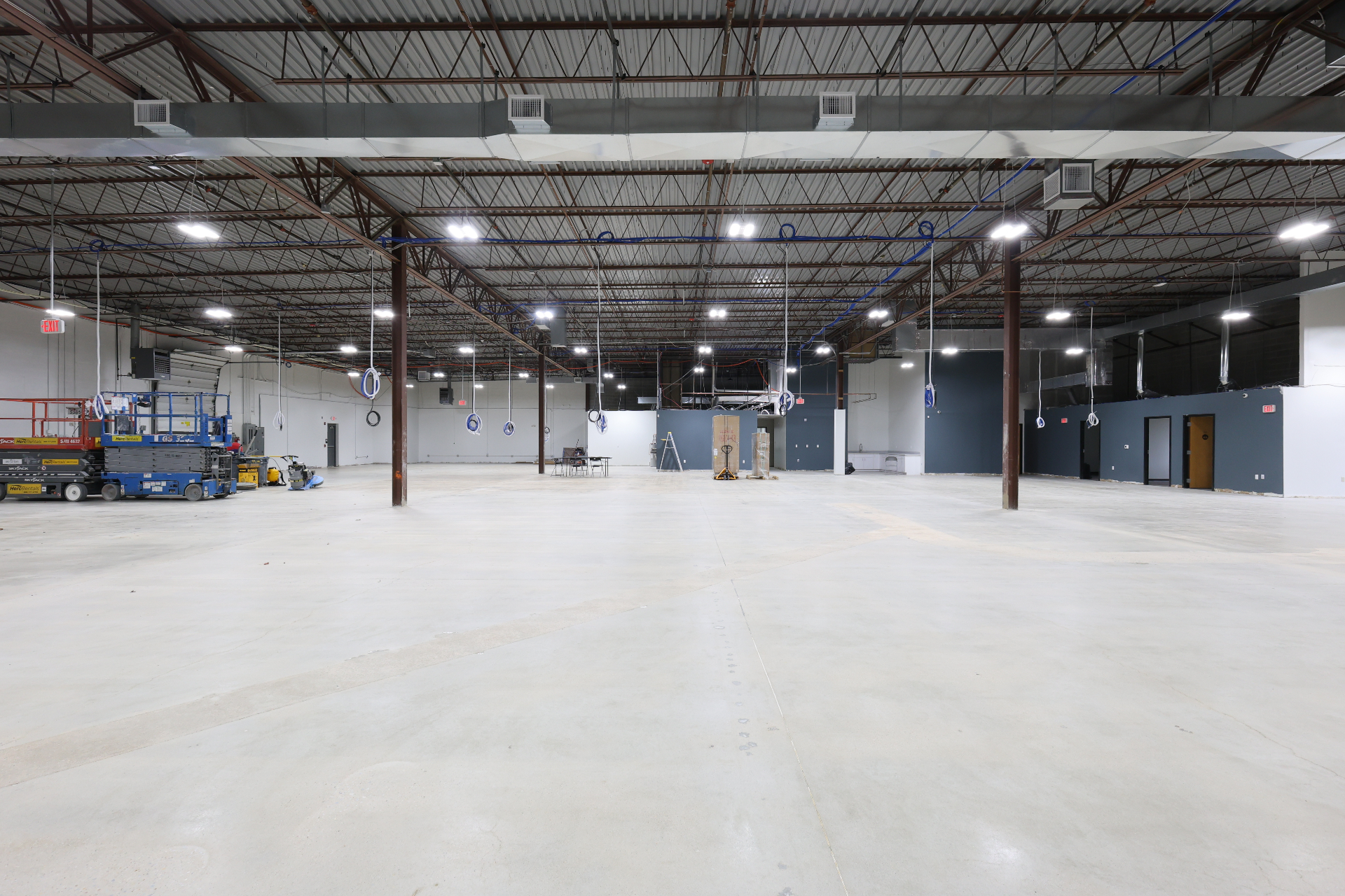 Warehouse interior mid-buildout with new lighting, painted accent wall, and polished slab